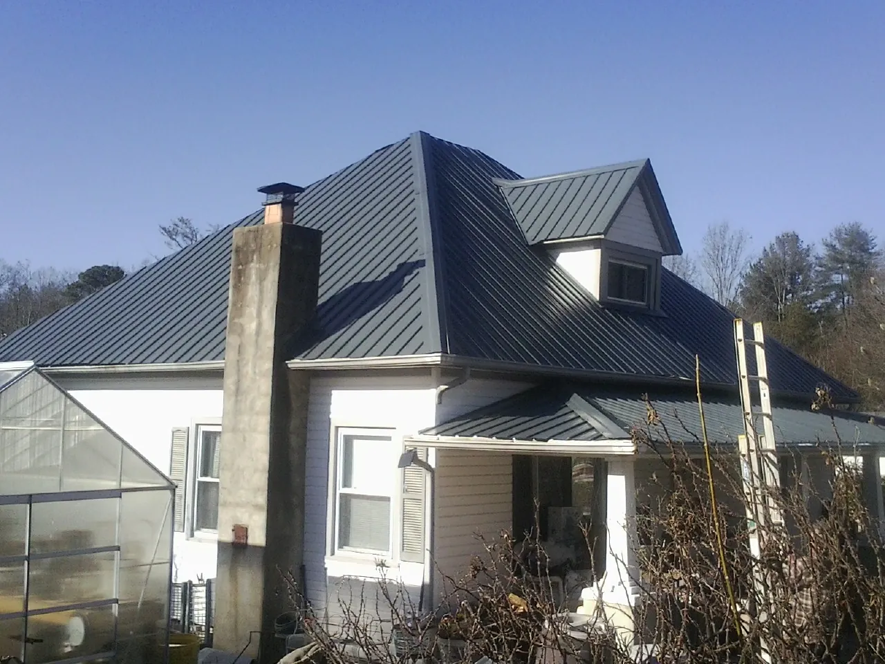 Dark blue standing seam metal roof on a white farmhouse with dormer — Slate & Tile Roof Repair by Roofing Brothers in Cochrane