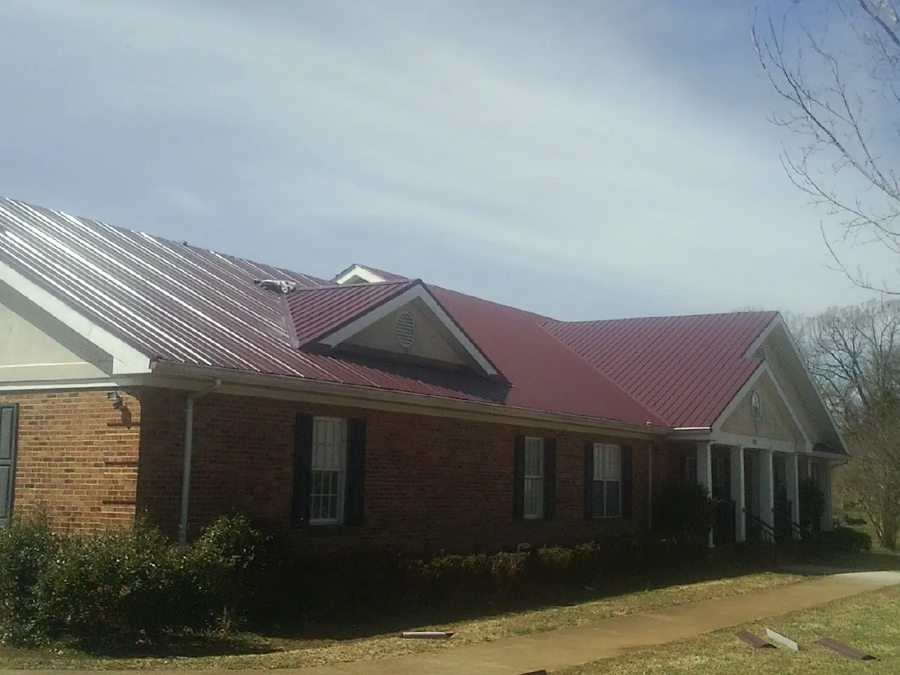 Red metal roof with gabled entries on a long brick building, from a Hail Damage Roof Repair job in Cochrane