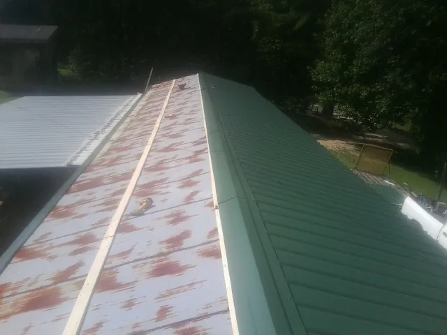 Old rusted panels beside newly installed green metal roofing — Wind Damage Roof Repair by Roofing Brothers in Cochrane