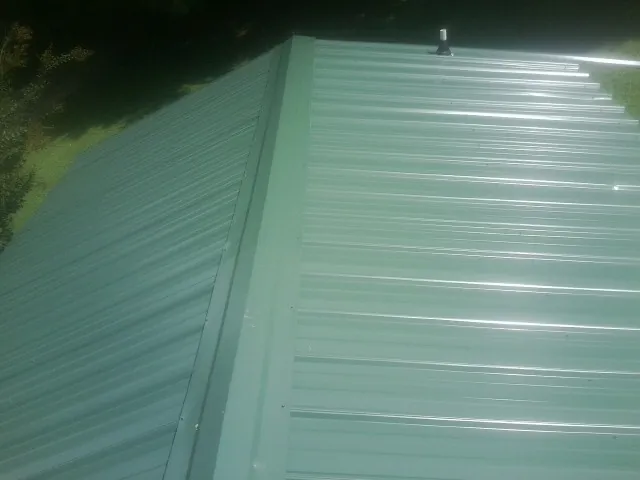 New green metal panels meeting at the ridge of a roof — Flat Roof Repair work by our crew in Cochrane