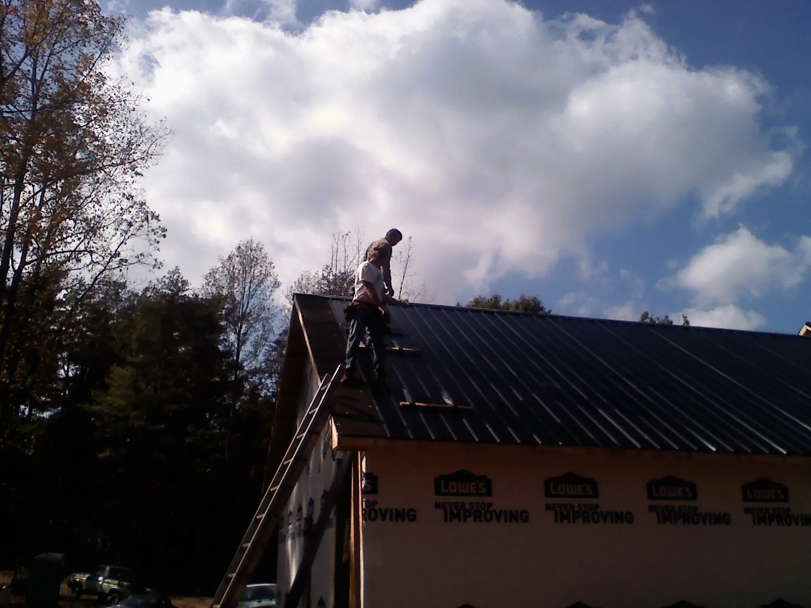 Roofer fastening dark metal panels high against a cloudy sky, from a Roof Inspection job in Cochrane