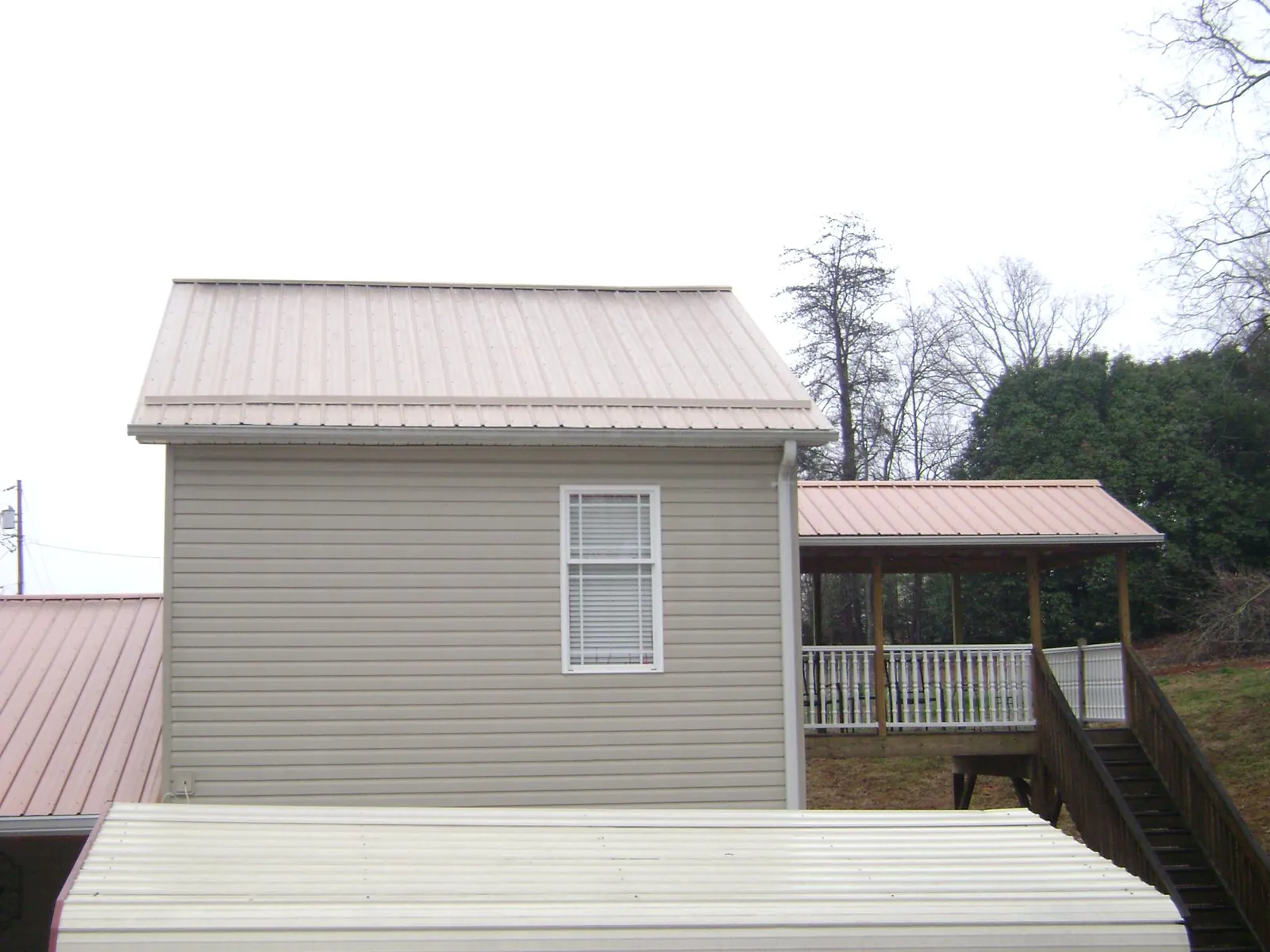Tan metal roofs on a two story addition and attached porch, from a Roof Replacement job in Cochrane