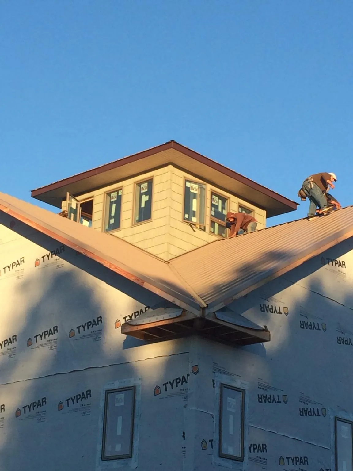 Roofers working around a rooftop cupola on a new metal roof at sunset — Roof Waterproofing in Cochrane by Roofing Brothers